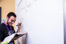 Mathematics on a white board with a tutor smiling while writing