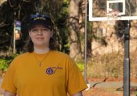 Maddy Brown in a t-shirt and baseball cap stands on a basketball court.